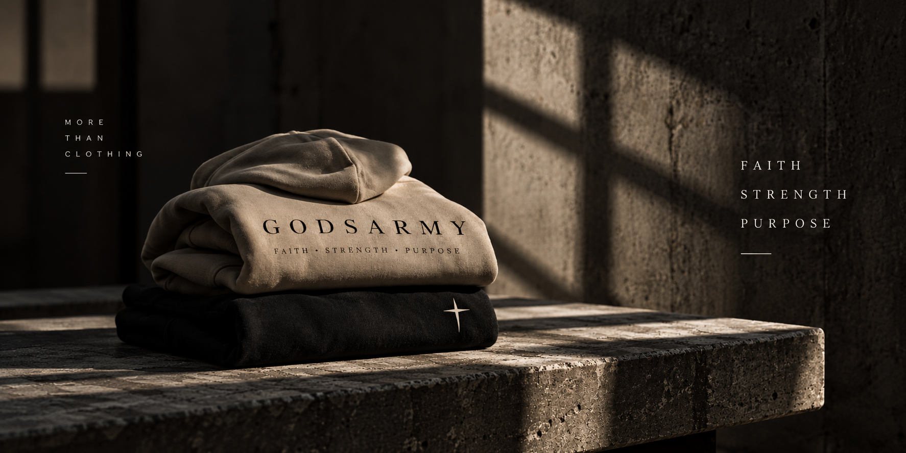 Folded bone and black GODSARMY hoodies stacked on a stone bench in warm light